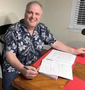 A person in floral shirt smiling holding pen